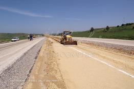 Image du Maroc Professionnelle de  Travaux sur la voie en construction sidi el Yamani-Asilah au point kilométrique 8 vers Tanger, installation de la première épaisseur de la couche de revêtement de la chaussée. Des ouvriers à l'aide d'un engin spécial TP travail sur le TPC terre plein central, l'autre engin au fond à gauche assure la mise en place de la GNT (grave non traité), Mercredi 12 Juin 2002. (Photo / Abdeljalil Bounhar) 